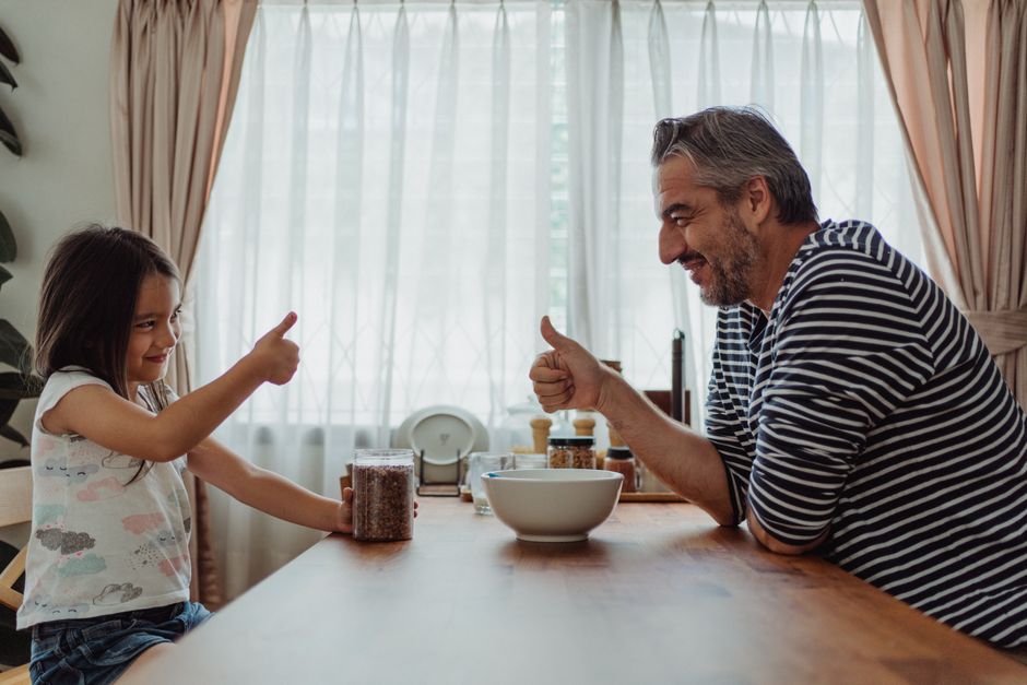 Father and daughter bonding over breakfast, sharing smiles and gestures in a cozy indoor setting.