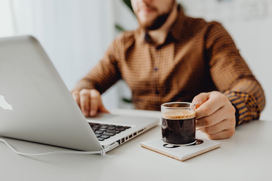 Adult man working remotely on laptop with coffee in a home office setting.