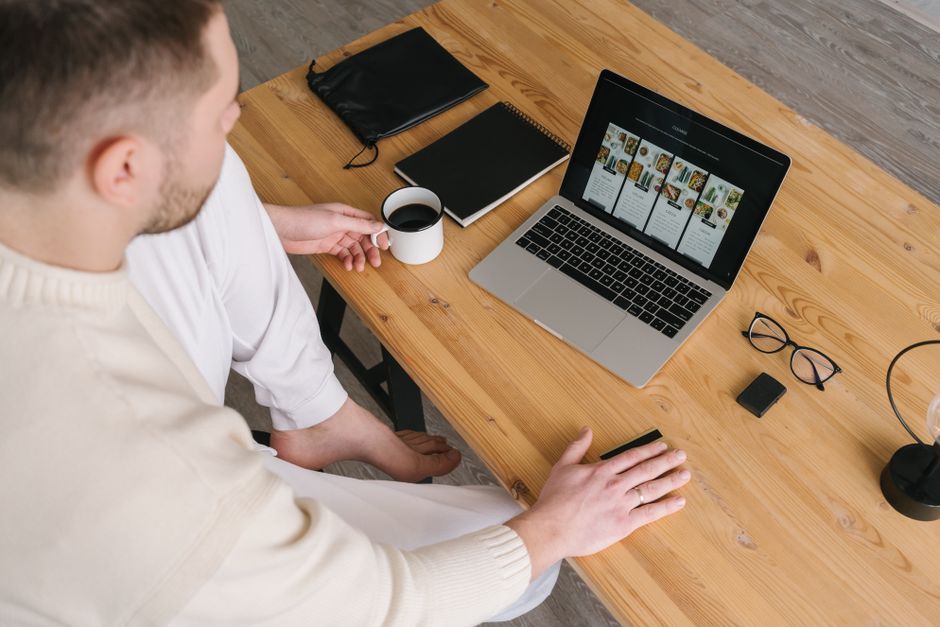 Adult man browsing online shopping site on laptop with coffee, at a wooden desk.