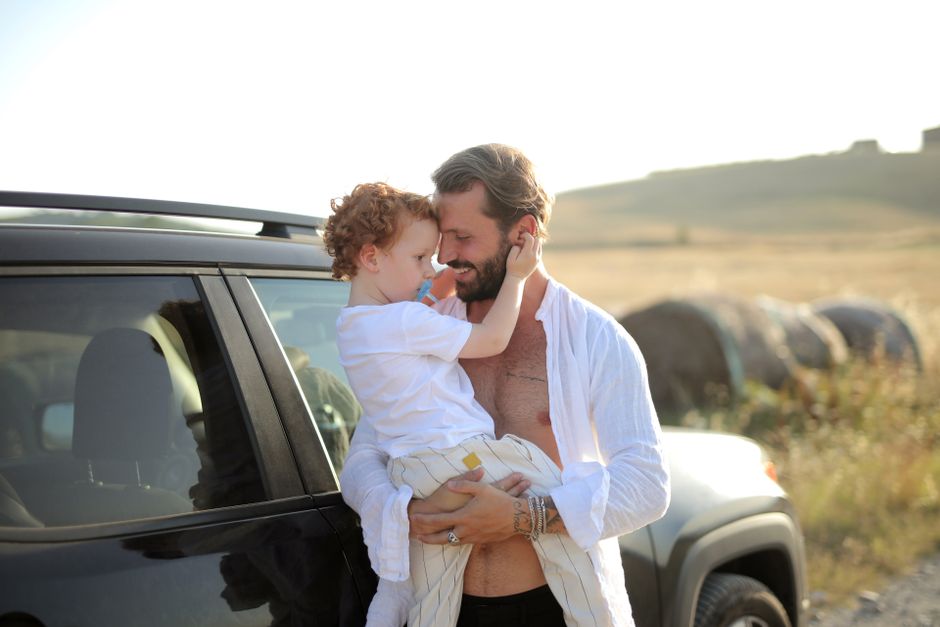 A loving father and son embrace joyfully in a sunny countryside setting by their car.