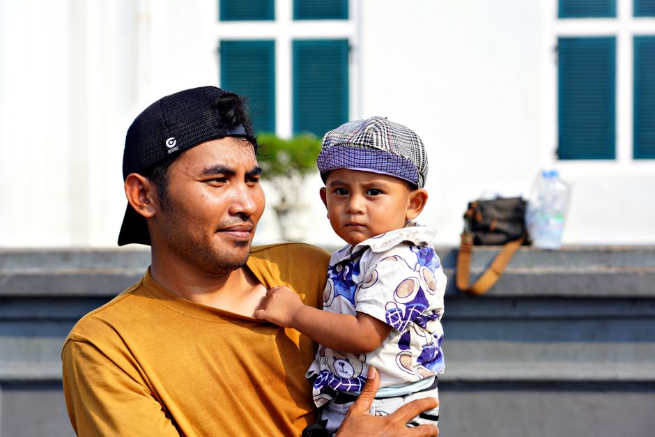 A father holds his young son while enjoying a sunny day outdoors.