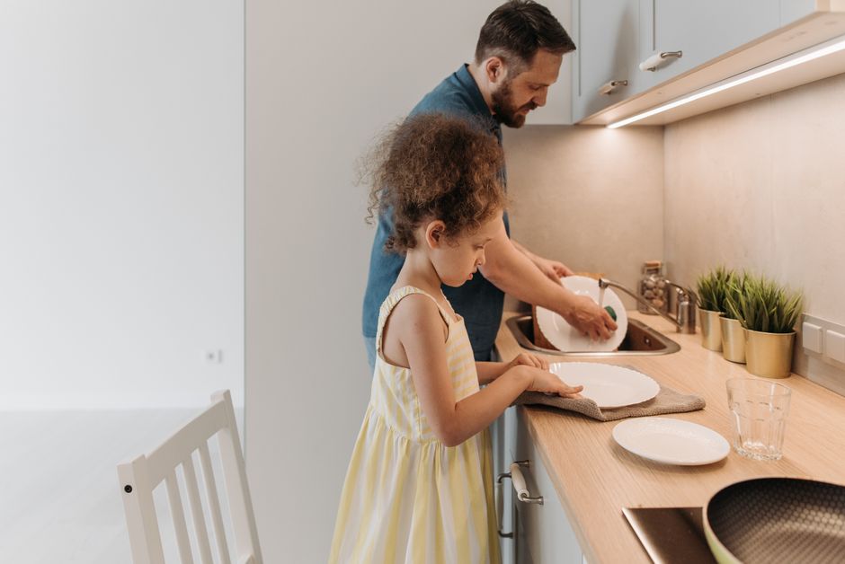 Father and daughter bonding while washing dishes together in a modern kitchen.