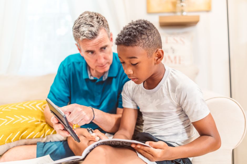 Father and son studying together at home, focused on learning with a tablet and notebook.