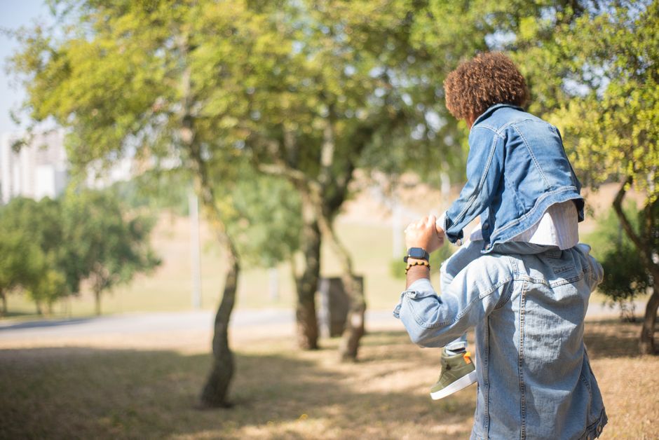 A father carries his son on his shoulders in a sunny park.