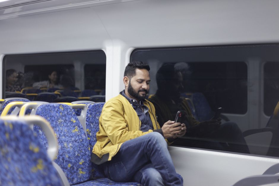 A man in a yellow jacket uses his smartphone while riding on a train.
