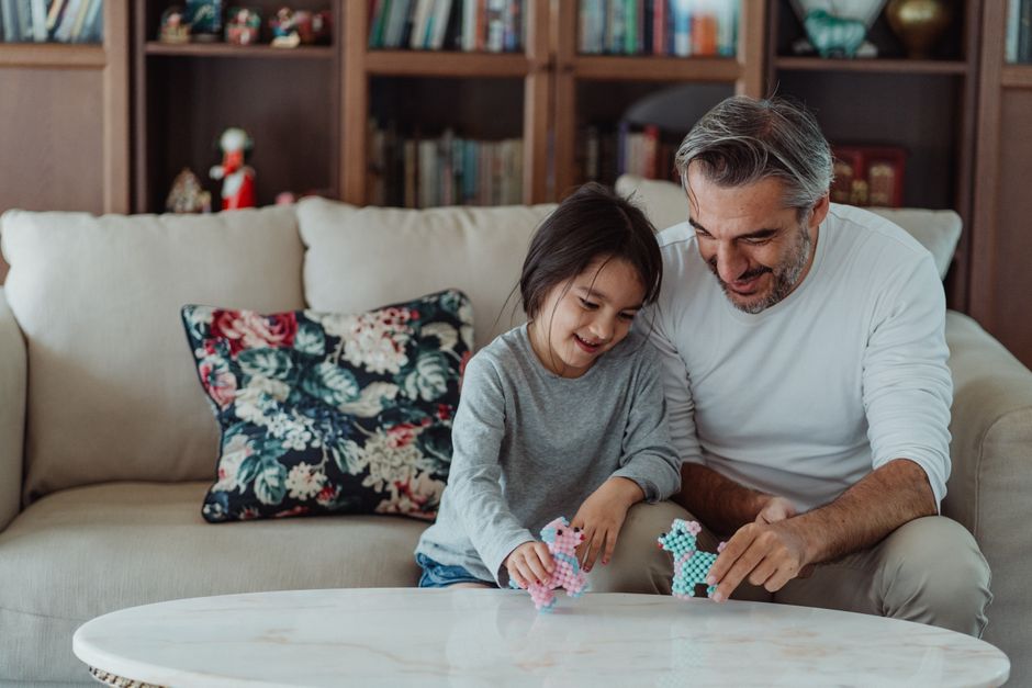 Father and daughter enjoy quality time playing with toy ponies on the living room sofa.